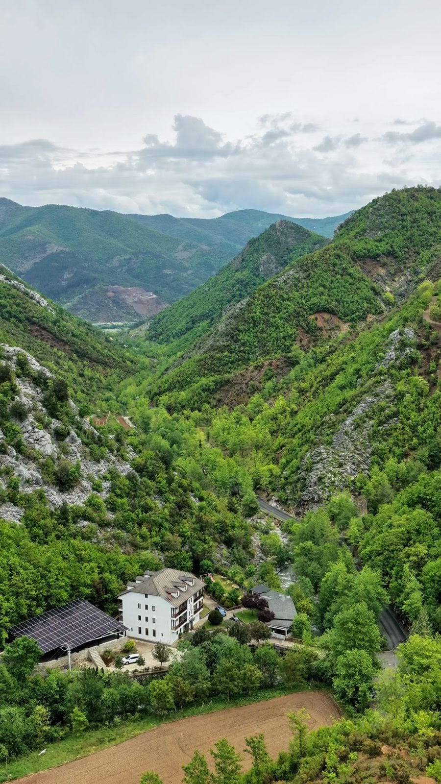 The side of the hotel against a steep wooded hillside and rock face