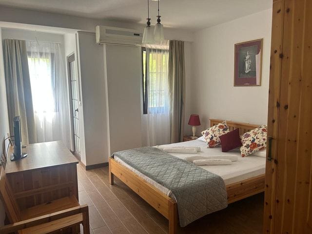 Double room with a wooden bed, patterned cushions and two windows with light curtains