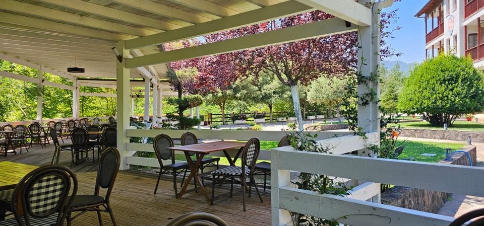 Shaded wooden terrace with café tables, looking out over the garden and trees